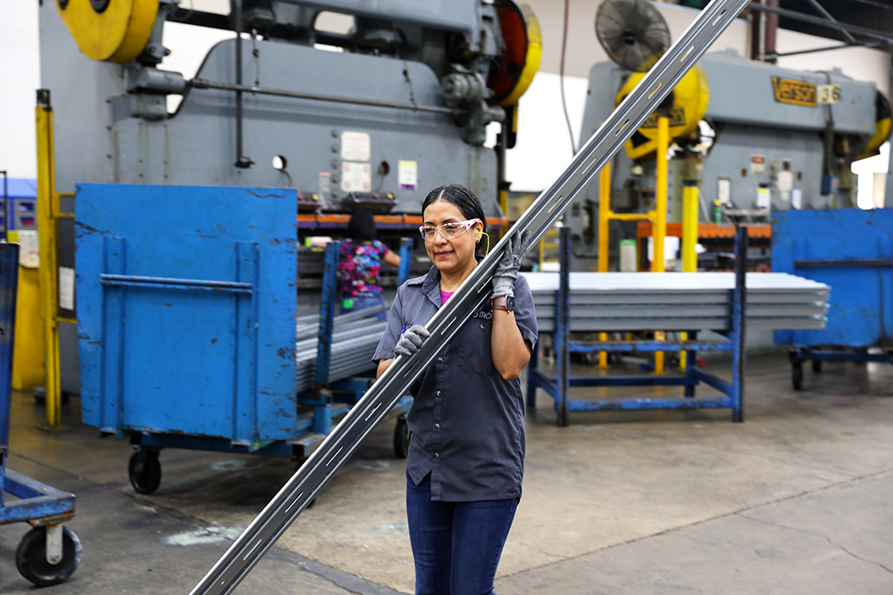 Solar worker carrying a metal tube in a manufacturing facility.